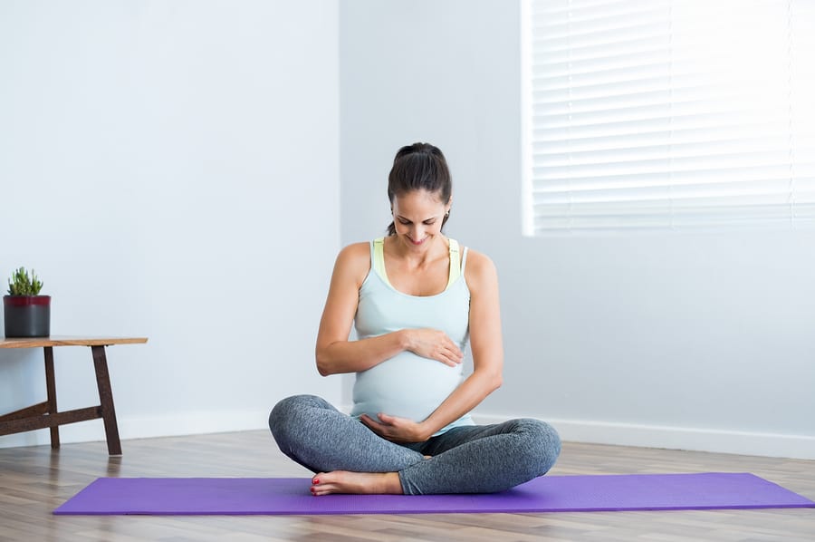 Pregnant woman sitting in lotus position on exercise mat